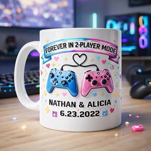 Può includere: Tazza in ceramica bianca con manico, con un design di controller per videogiochi blu e rosa. La tazza presenta il testo "FOREVER IN 2-PLAYER MODE", i nomi "NATHAN & ALICIA" e la data "6.23.2022".