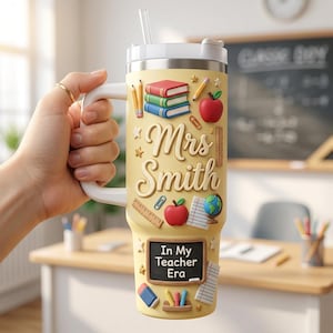 May include: A yellow insulated tumbler with a white handle and lid featuring a straw. The design includes stacked books, pencils, apples, a globe, a ruler, and a chalkboard graphic with the text "Mrs. Smith" and "In My Teacher Era."
