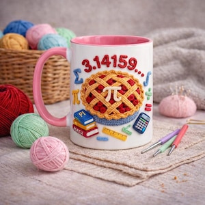 Puede incluir: Taza de cerámica blanca con asa y borde rosa, decorada con un diseño de tarta de ganchillo y los números 3.14159. La taza también presenta símbolos matemáticos y libros de ganchillo. Una cesta de ovillos de lana está en el fondo.