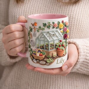 May include: White ceramic mug with a pink interior and handle, featuring a detailed garden scene. The design includes a greenhouse, flowers, a bird, and the name "Lily". The mug is decorated with gardening tools and a basket of fruit.
