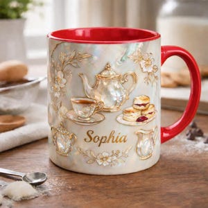May include: A ceramic mug with a red interior and handle, featuring a pearlized finish. The mug is adorned with embossed tea party elements, including a teapot, teacup, and scones. The name "Sophia" is written in gold script.
