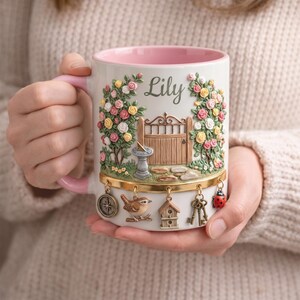 May include: A white ceramic mug with a pink interior and handle, featuring a garden scene with roses, a gate, and the name "Lily." Decorative charms include a compass, bird, birdhouse, keys, and a ladybug.