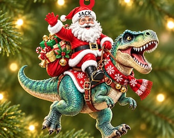 May include: A Christmas tree ornament featuring Santa Claus riding a green Tyrannosaurus Rex. Santa wears a red suit with a hat labeled JACK and carries a sack of gifts. The dinosaur wears a red and white snowflake patterned scarf and a brown saddle.