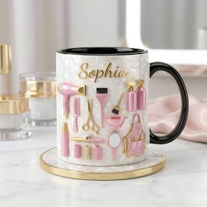 May include: A white and black mug with the name "Sophia" in gold lettering. The mug is decorated with pink and gold hair styling tools. The mug sits on a matching coaster with a gold rim. The handle is black.