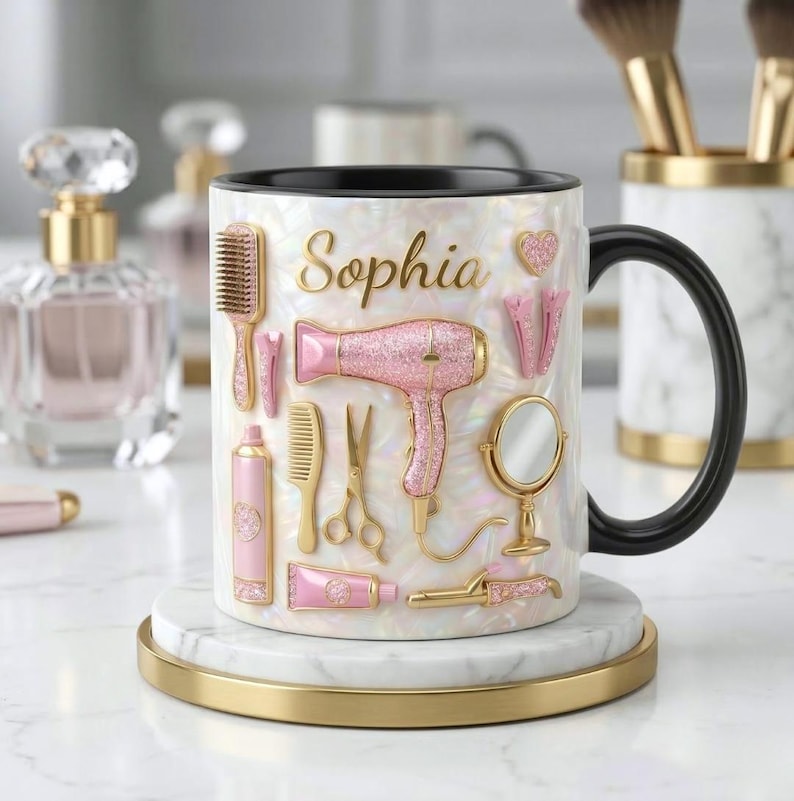 May include: White ceramic mug with a black handle, featuring the name "Sophia" in gold script. The mug is decorated with pink and gold hair styling tools, including a hairdryer, comb, and scissors. The mug sits on a white and gold coaster.