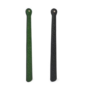 May include: Two shoe horns. One is green, the other is black. Both are made of leather and have a loop at the top for hanging. The green shoe horn has a textured surface, while the black one has a smooth surface.
