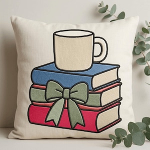 Può includere: Un cuscino quadrato color bianco sporco con un ricamo raffigurante una pila di tre libri in blu, verde e rosso. Un fiocco verde chiaro è legato attorno al libro centrale e una tazza da caffè beige è posta sopra la pila con contorni neri.