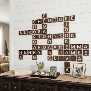 May include: A wall-mounted display of wooden Scrabble tiles spelling out names such as Theodore and Aurora. A dark wooden cabinet below holds a tray with stones and a framed family photograph.