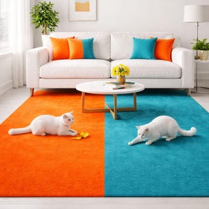 Op de afbeelding: Een moderne woonkamer met een witte bank, oranje en turquoise kussens en een ronde salontafel. Het tapijt is verdeeld in oranje en turquoise helften, met twee witte katten erop.