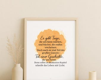 May include: A framed print with a light wood frame. The print features a quote in German with an orange watercolor-style background. A small vase with dried plants and candles are on the table.