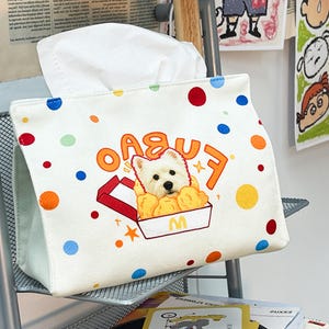 以下が含まれることがあります： 白い生地のティッシュボックスカバー。カラフルな水玉模様。白い犬がファストフードの箱に入った刺繍画像と「FUBAO」の文字が特徴です。ティッシュボックスカバーは長方形で、ティッシュを出すためのスロットがあります。