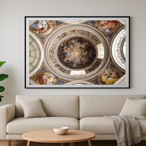 May include: A framed print of a detailed ceiling fresco, featuring a central circular design with figures and ornate details. The artwork is set against a neutral wall above a beige sofa, creating a classic aesthetic.