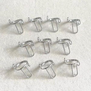 May include: A collection of nine silver-colored metal pendant trays. Each tray features a circular bezel with two small loops and a U-shaped bail. The trays are arranged on a light-colored surface.