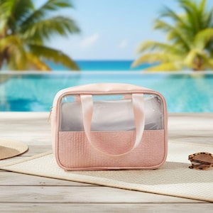Könnte beinhalten: Eine rosa Kosmetiktasche mit transparentem Frontpanel und strukturiertem Unterteil. Die Tasche hat einen Reißverschluss, einen oberen Griff und liegt auf einer gewebten Matte. Sonnenbrillen liegen neben der Tasche.