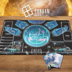 May include: A black Gundam card game playmat with a futuristic design, featuring a central circular graphic and labeled zones. The mat includes the Gundam logo and Japanese text. Three playing cards are visible on a wooden surface.