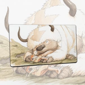 Op de afbeelding: Een rechthoekige muismat met een aquarel illustratie van een personage uit Avatar: The Last Airbender. De afbeelding toont een persoon die rust op een groot, pluizig, bisonachtig wezen. Het kleurenpalet bevat tinten bruin, beige en wit.