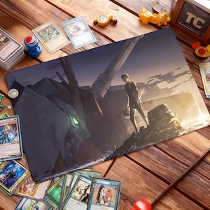 May include: A rectangular gaming mousepad featuring a detailed anime-style illustration of a futuristic robot and a person standing on a rocky surface. The color palette includes shades of gray, blue, and green. Trading cards are scattered around the mousepad.