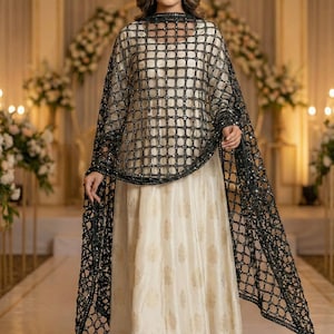 May include: An elegant cream-colored gown with gold floral patterns, paired with a black, open-weave shawl. The shawl is adorned with sparkling embellishments. The outfit is suitable for formal events.