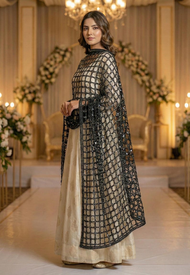 May include: A formal cream-colored dress with a black, grid-patterned overlay. The overlay features sparkling embellishments and long sleeves with fringe. The dress is suitable for special occasions and events.