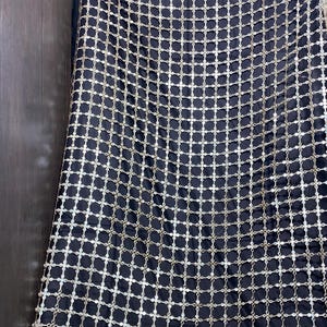 May include: Black fabric with a grid pattern of silver-colored, circular embellishments. The fabric is draped, creating folds and shadows. The overall effect is one of luxury and texture, suitable for evening wear or decorative purposes.