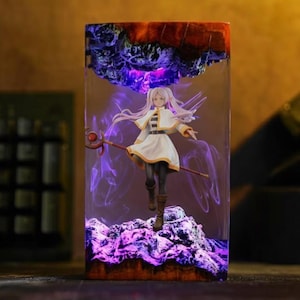 Puede incluir: Una taza de cerámica blanca con un asa negra y el texto "But First, Coffee" en negrita negra. La taza se encuentra sobre un fondo borroso, sugiriendo un ambiente acogedor.