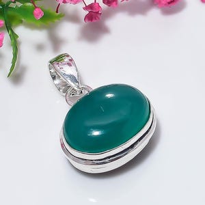 May include: A polished oval green gemstone pendant set in a smooth silver metal frame. The pendant features a rounded, cabochon-cut green stone securely held within a silver bezel, complete with a silver bail at the top for attachment to a chain.