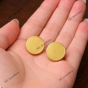 Op de afbeelding: Een paar ronde oorknopjes met een matte gouden afwerking en een glad, plat oppervlak. De tekst HD Jewellers is meerdere keren zichtbaar op de afbeelding. Deze oorbellen hebben een eenvoudig, rond ontwerp met een dunne, opstaande rand.