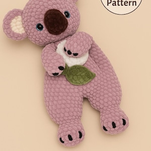 May include: A mauve, brown, and white crochet koala bear. The koala has blue eyes, a brown nose, and a green leaf detail. The image includes a circular graphic that reads "PDF Crochet Pattern".