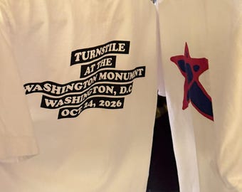 Puede incluir: Una camiseta blanca con texto negro en la parte posterior que dice TURNSTILE AT THE WASHINGTON MONUMENT WASHINGTON, D.C. OCT 24, 2026. Una segunda camiseta blanca es visible al lado, mostrando un gráfico de estrella roja y azul.