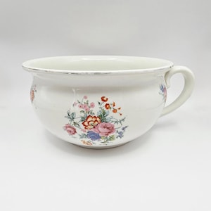 May include: A white ceramic mug with a black handle and the text "But First, Coffee" in a black, handwritten-style font. The mug is on a white surface.