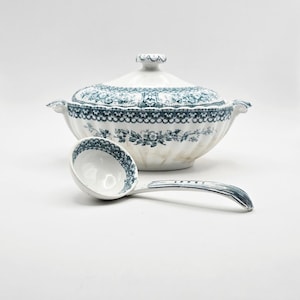 May include: A white ceramic tureen with a lid and matching ladle, both decorated with a dark blue floral and scalloped pattern. The tureen features two side handles and a fluted base, while the ladle has a deep bowl and a curved handle.