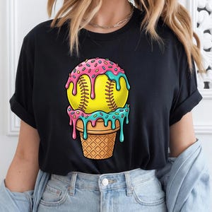 May include: Black t-shirt featuring a softball designed as an ice cream cone. The softball is yellow with pink and blue dripping frosting and sprinkles, set atop a waffle cone. The shirt is a casual wear item.