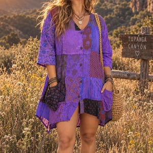 May include: A purple patchwork tunic dress featuring a V-neckline, three-quarter length sleeves, and two front pockets. The garment is constructed from various fabric panels with floral and geometric patterns, secured by a central row of buttons.