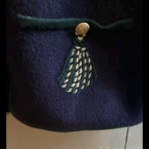 Puede incluir: Primer plano de una prenda azul marino con un ribete verde oscuro y una borla decorativa. La borla es blanca y verde oscuro, y la prenda tiene un bot&oacute;n dorado.