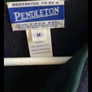 Puede incluir: Primer plano de un su&eacute;ter azul marino con ribete verde. La etiqueta dice "PENDLETON" en letras blancas sobre fondo azul, con "100% VIRGIN WOOL" debajo. Una etiqueta blanca indica la talla "M".