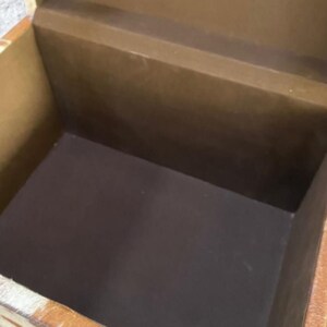 K&ouml;nnte beinhalten: Eine offene, rechteckige Aufbewahrungsbox mit braunem Innenraum und hellbraunem &Auml;u&szlig;eren. Die Box hat einen dunkelbraunen Innenboden und ein hellbraunes &Auml;u&szlig;eres mit einem gemusterten Design. Die Box ist aus Holz.