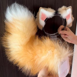 Puede incluir: Una cola de zorro esponjosa, naranja y blanca, y una diadema a juego con orejas. La cola es grande y tupida, con un degradado de colores. La diadema tiene dos orejas con detalles interiores rosas.