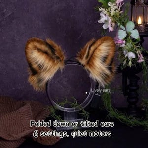 Puede incluir: Un par de orejas de animal de piel sintética marrón y negra unidas a una diadema circular. Las orejas presentan fibras largas y suaves con puntas oscuras. El texto en la imagen dice: Folded down or tilted ears, 6 settings, quiet motors, Lively ears.