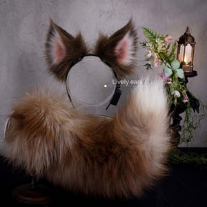 May include: A set of brown and white faux fur animal ears on a black headband and a matching long, fluffy brown and white faux fur tail. The text "Lively ears" is printed in white next to the headband. The ears feature pink inner accents.