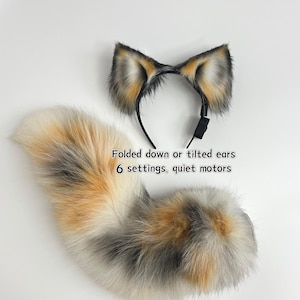 Può includere: Un set di orecchie da animale in pelliccia sintetica su un cerchietto nero e una coda soffice abbinata. Le orecchie presentano un mix di pelo arancione, grigio e bianco. Il testo recita: Folded down or tilted ears, 6 settings, quiet motors.