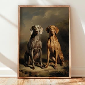 Op de afbeelding: Een ingelijste print met twee honden, een grijze Weimaraner en een roodbruine Vizsla, die naast elkaar zitten. De honden zijn afgebeeld in een klassieke stijl tegen een achtergrond van een bewolkte lucht en gebladerte. De lijst is lichtbruin.