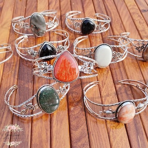 Puede incluir: Varios brazaletes de plata con diferentes piedras preciosas engastadas. Las piedras son de forma ovalada, de lágrima y redondas, en colores como negro, rojo, verde y blanco. Los brazaletes tienen detalles florales.