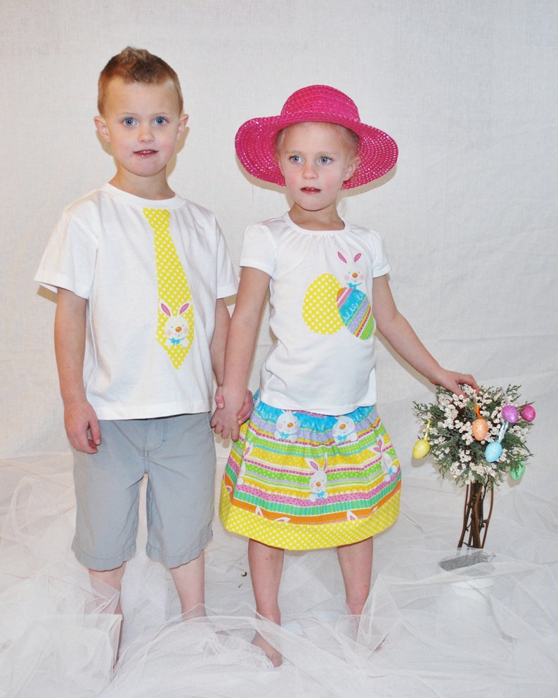 Puede incluir: Dos ni&ntilde;os con atuendos de Pascua. Uno lleva una camiseta blanca con un dise&ntilde;o de corbata amarilla y pantalones cortos grises. El otro lleva una camiseta blanca, una falda colorida y un sombrero rosa. Se est&aacute;n dando la mano.
