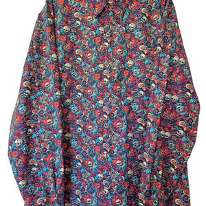 May include: Long-sleeved button-down shirt featuring a colourful pattern of skulls, flowers, and swirling designs in red, blue, and purple. The shirt is displayed on a black hanger against a white background.