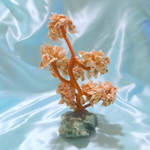 May include: A decorative tree made of seashells with a green stone base. The tree is made of small, white seashells and has a brown wire frame.