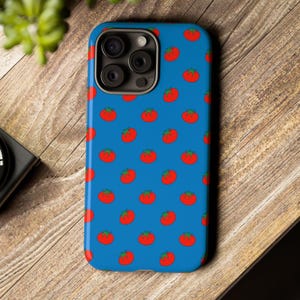 Puede incluir: Una funda de teléfono azul con un patrón repetido de tomates rojos con tallos verdes. La funda tiene un acabado brillante y un recorte para la cámara. El diseño es un accesorio divertido y lúdico para un teléfono inteligente.