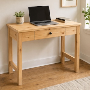 May include: A light-coloured wooden desk with a drawer and a black knob. A laptop sits on the desk, alongside a small potted plant and a stack of books. The desk has a simple design and is supported by four sturdy legs.