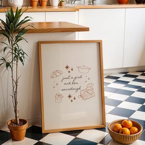May include: A framed print with the text "just a girl and her sourdough" and illustrations of bread and cooking tools. A potted plant and a basket of oranges sit nearby. The floor has a black and white checkered pattern.