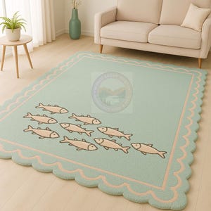 May include: A rectangular, light green rug with a scalloped edge and a pink border. The rug features a school of beige fish swimming across the surface. The rug is placed on a light wood floor.