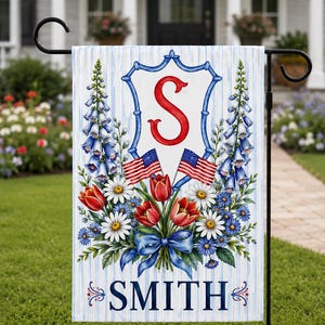 May include: A garden flag with a patriotic theme. The flag features a blue and white striped background with a floral arrangement of red tulips, white daisies, and blue flowers. The flag also displays the name "SMITH" and a red "S" initial.